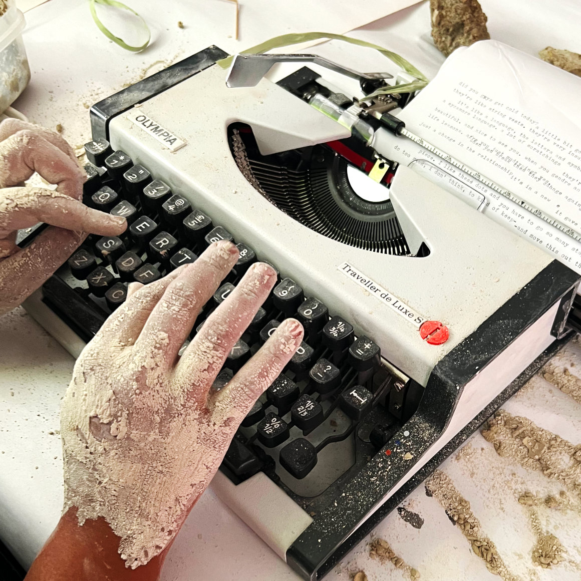 Close up of hands covered in dried clay typing on a mechanical typewriter